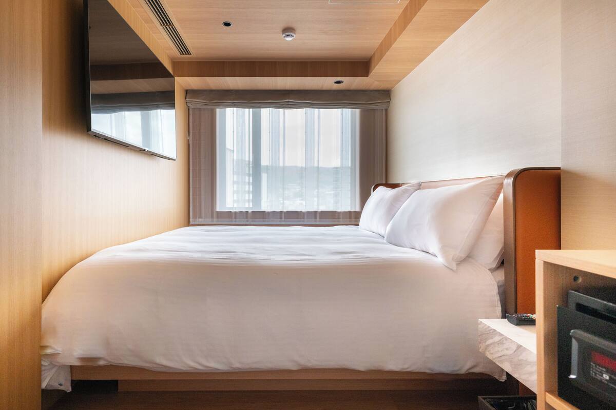 Una habitación de hotel con una cama, televisión, ventana con cortinas y techo de madera.