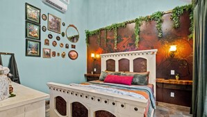 A bed with a decorative headboard, a wall with framed pictures, and a wall-mounted light fixture. - Romantic Storybook Cottage Hot Tub No Cleaning Fee (Lonoke)