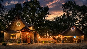 A rustic cabin with a stone facade, a wooden door, and a circular window. - Romantic Storybook Cottage Hot Tub No Cleaning Fee (Lonoke)