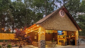 A rustic cabin-style building with a stone facade, outdoor seating area, and a television screen. - Romantic Storybook Cottage Hot Tub No Cleaning Fee (Lonoke)
