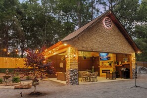 Un bâtiment de style rustique, rappelant une cabane, avec une façade en pierre, un espace extérieur aménagé pour s’asseoir et un écran de télévision.