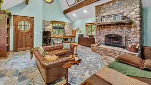A spacious living area with a stone fireplace, leather sofa, and a dining area with a view of the outdoors.