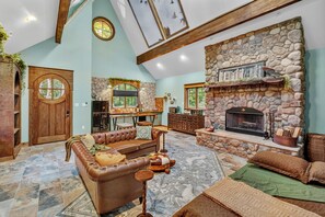 A spacious living area with a stone fireplace, leather sofa, and a dining area with a view of the outdoors. - Romantic Storybook Cottage Hot Tub No Cleaning Fee (Lonoke)