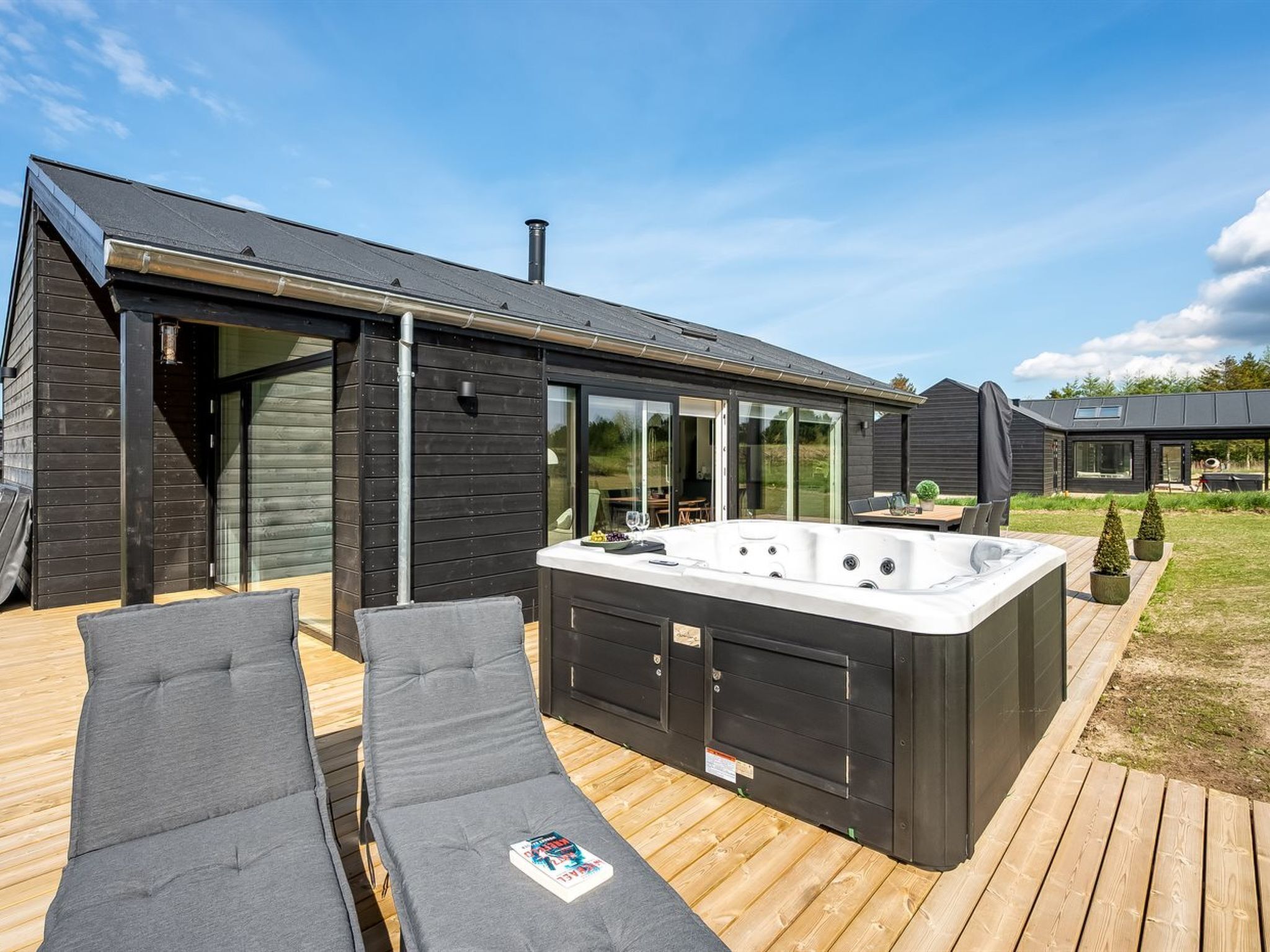 A modern house with a hot tub, wooden deck, and lounge chairs.