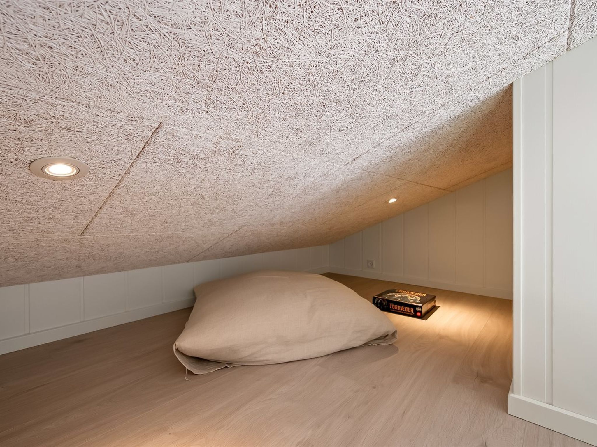 Une chambre mansardée avec un plafond en pente, un plancher en bois, un lit simple et une petite bibliothèque.
