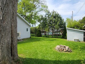 A residential backyard with a white house, a tree, a grassy lawn, and a pile of bricks.