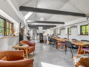 Ein geräumiger Raum mit einem langen Tisch, Ledersesseln, einem Kamin und einer Küchenzeile.