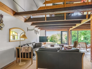 Ein modernes Wohnzimmer mit hoher Decke, einem Sofa, einem Couchtisch und Blick ins Freie.