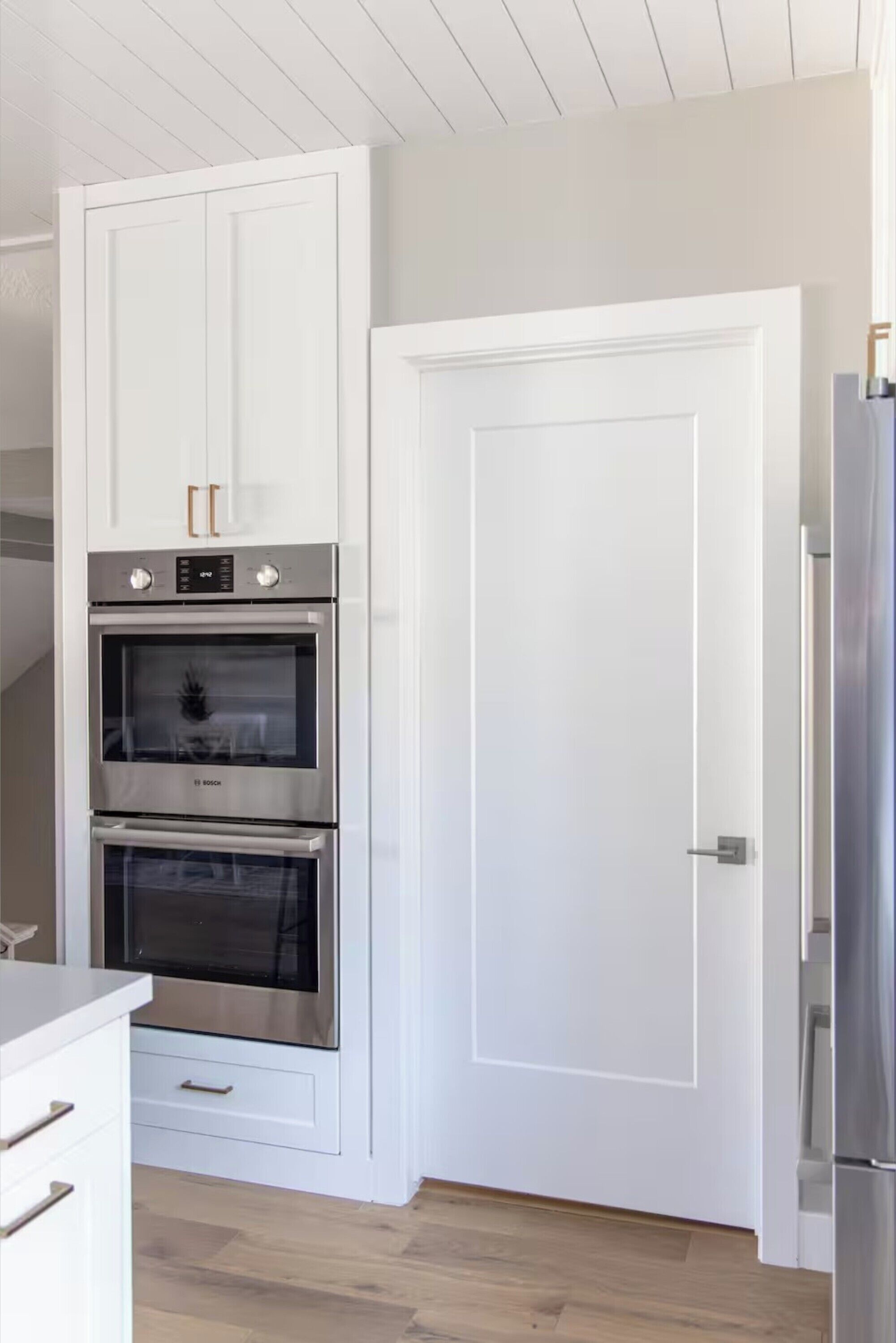 A kitchen with white cabinets, a double oven, and a white door.