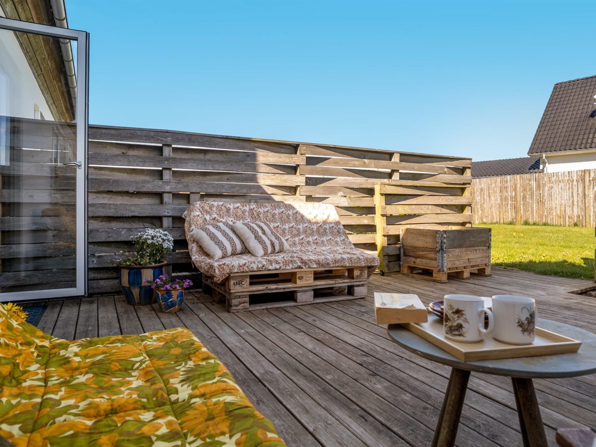 Eine Holzterrasse mit einer Couch, einem Tisch mit zwei Tassen und einem Topfpflanzen.