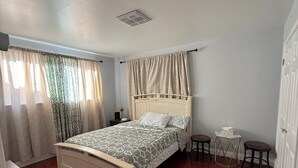 Un dormitorio con cama, una mesita, una silla y una ventana con cortinas.