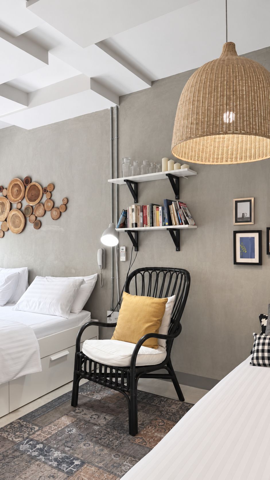 Ein modernes Schlafzimmer mit einem Bett, einem schwarzen Korbstuhl, einem Bücherregal und einer großen gewebten Pendelleuchte.