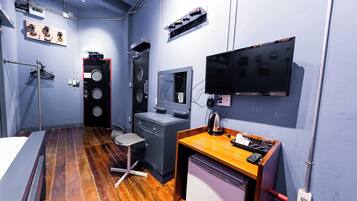 A compact hotel room with a wooden floor, a desk with a computer, a bed, and a TV mounted on the wall.