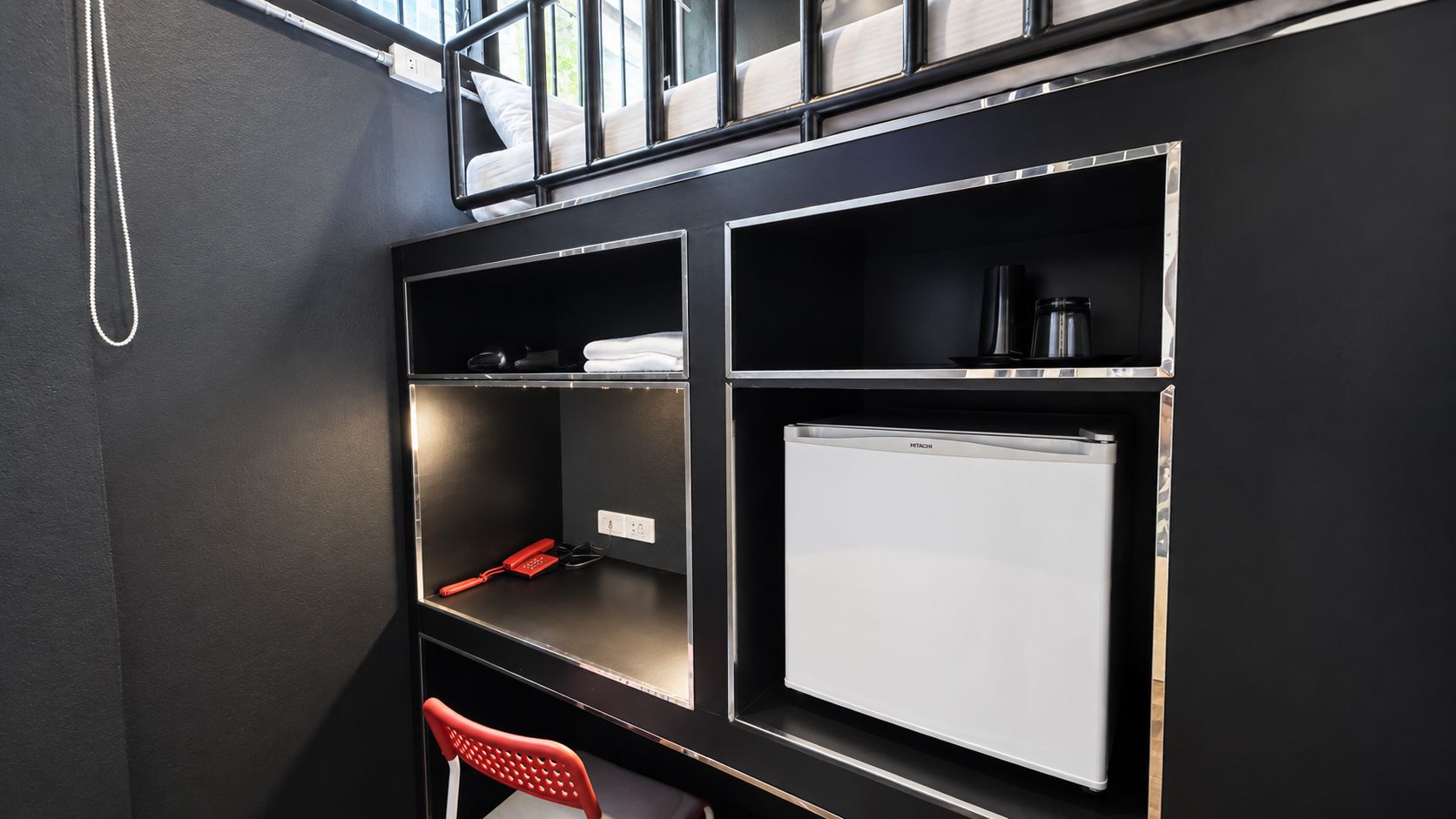 Une chambre d’hôtel de taille réduite, équipée d’un lit, d’un bureau et d’un mini-bar.