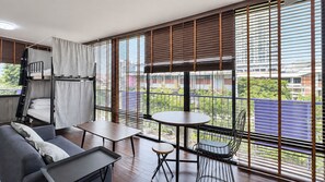 Una habitación moderna con literas, un sofá, una mesita y un balcón con vistas a edificios y zonas verdes.