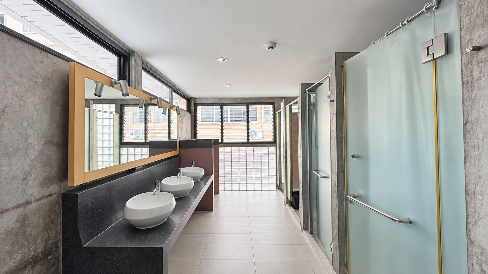 A modern bathroom with three sinks, a large mirror, and a glass shower enclosure.