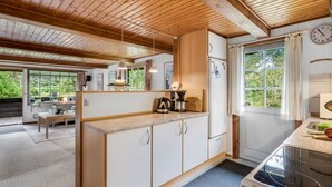 Une cuisine avec des poutres en bois, un poêle, des placards et une fenêtre avec des rideaux.