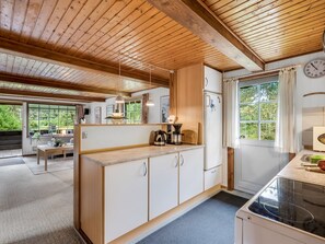 Una cocina con vigas de madera, estufa, armarios y una ventana con cortinas.