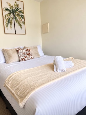 Quarto de hotel com cama, almofadas, cobertor, toalha e um quadro pendurado na parede.