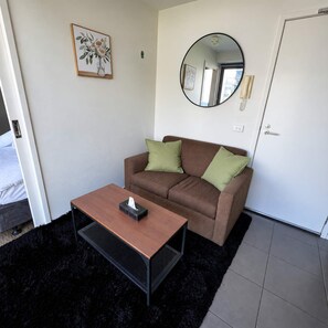 Ein Zimmer mit einem braunen Sofa, zwei grünen Kissen, einem runden Spiegel und einem kleinen Tisch mit einer Taschentuchbox.
