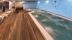 A modern indoor pool with a wooden deck, lounge chairs, and a large wall clock. - Platinum Towers by Interhome (Warsaw)