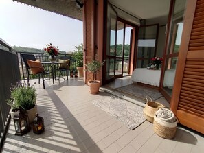 Een balkon met een tafel, stoelen, plantenbakken en een bed met uitzicht.