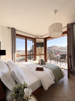 Een slaapkamer met een groot bed, uitzicht op een balkon met buitenmeubilair en een plafondlamp.