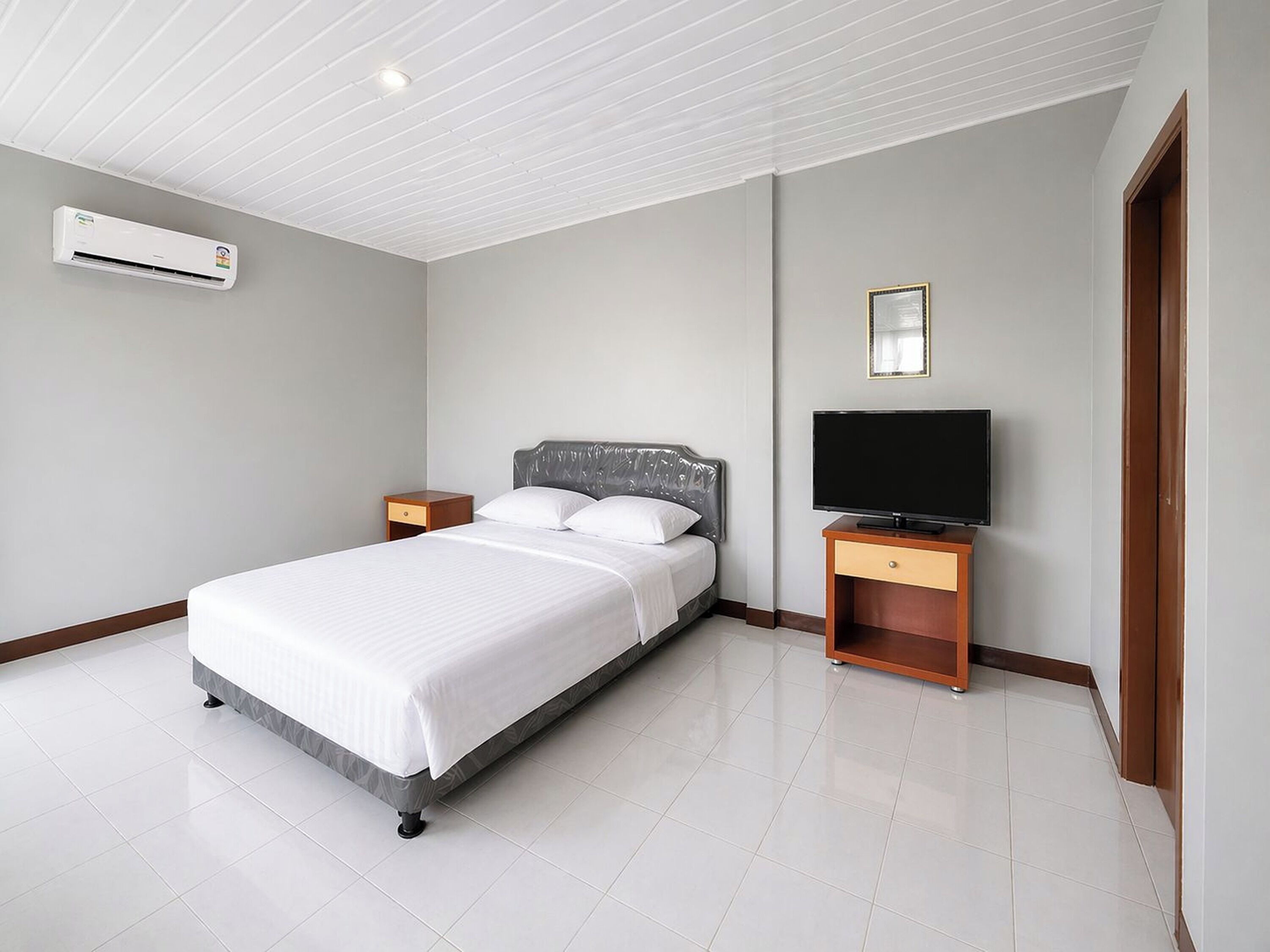 Een hotelkamer met een bed, een televisie, een nachtkastje en een airconditioning.