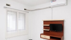 A room with a built-in TV shelf, a window with sheer curtains, and an air conditioning unit. - Nata Hotel Tasikmalaya (Tasikmalaya)
