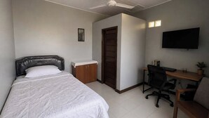 A bedroom with a bed, a desk, a chair, a TV, and a ceiling fan. - Nata Hotel Tasikmalaya (Tasikmalaya)