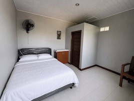 Un dormitorio con cama, armario de madera, puerta, ventilador y una pequeña imagen en la pared.