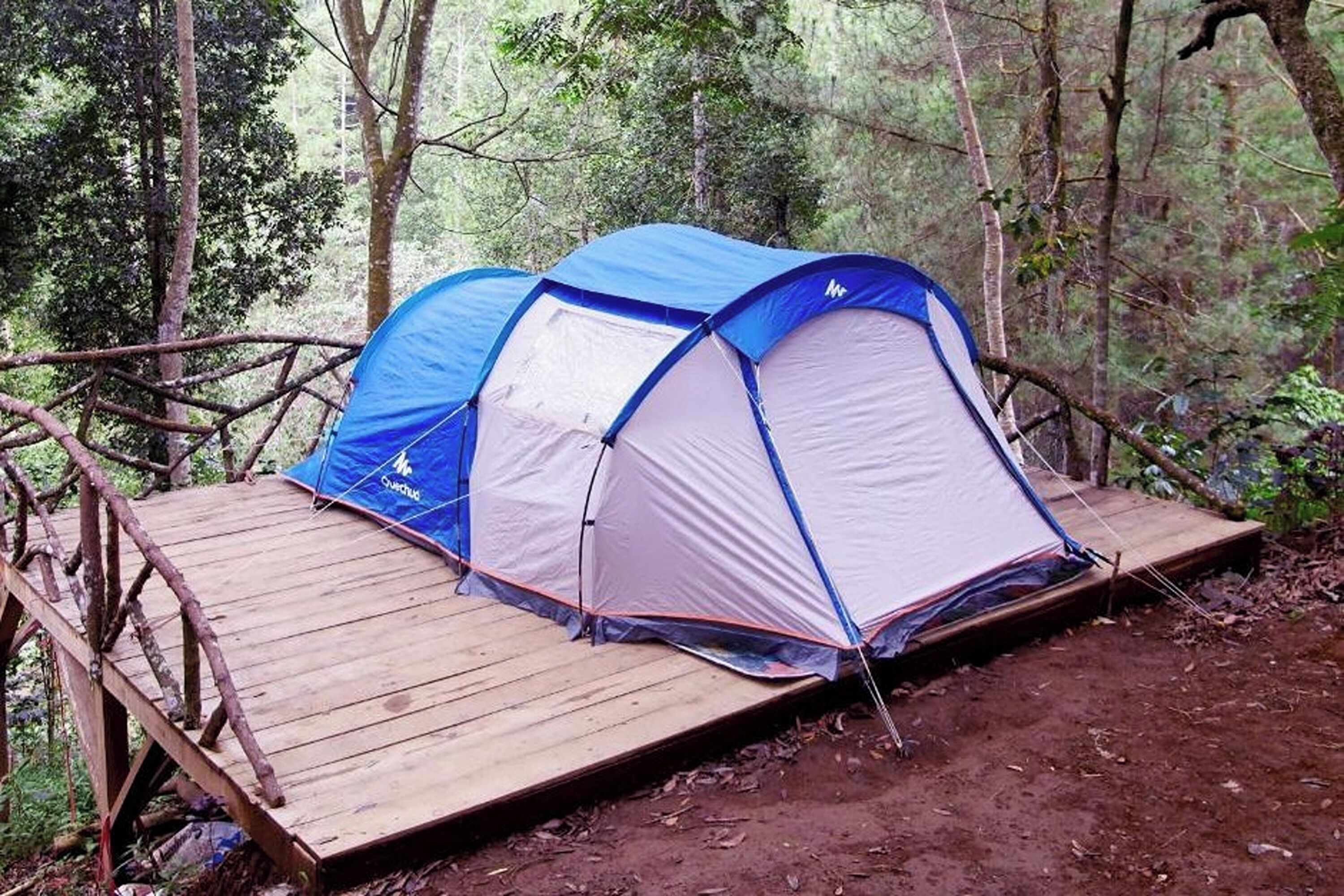 A blue and white tent on a wooden platform in a forest.