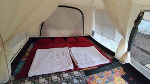 Una carpa con una cama, cojines rojos y un tapete colorido en el suelo.