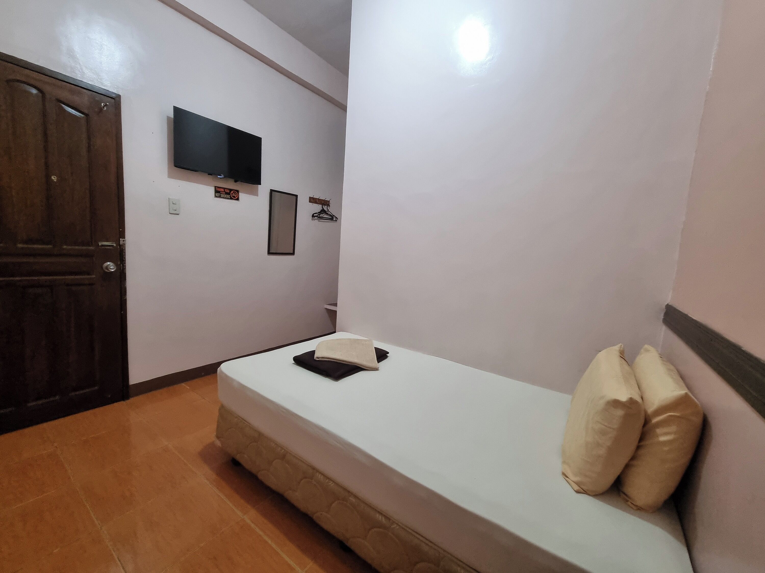 A bedroom with a single bed, a television on the wall, a door, and a small framed picture.