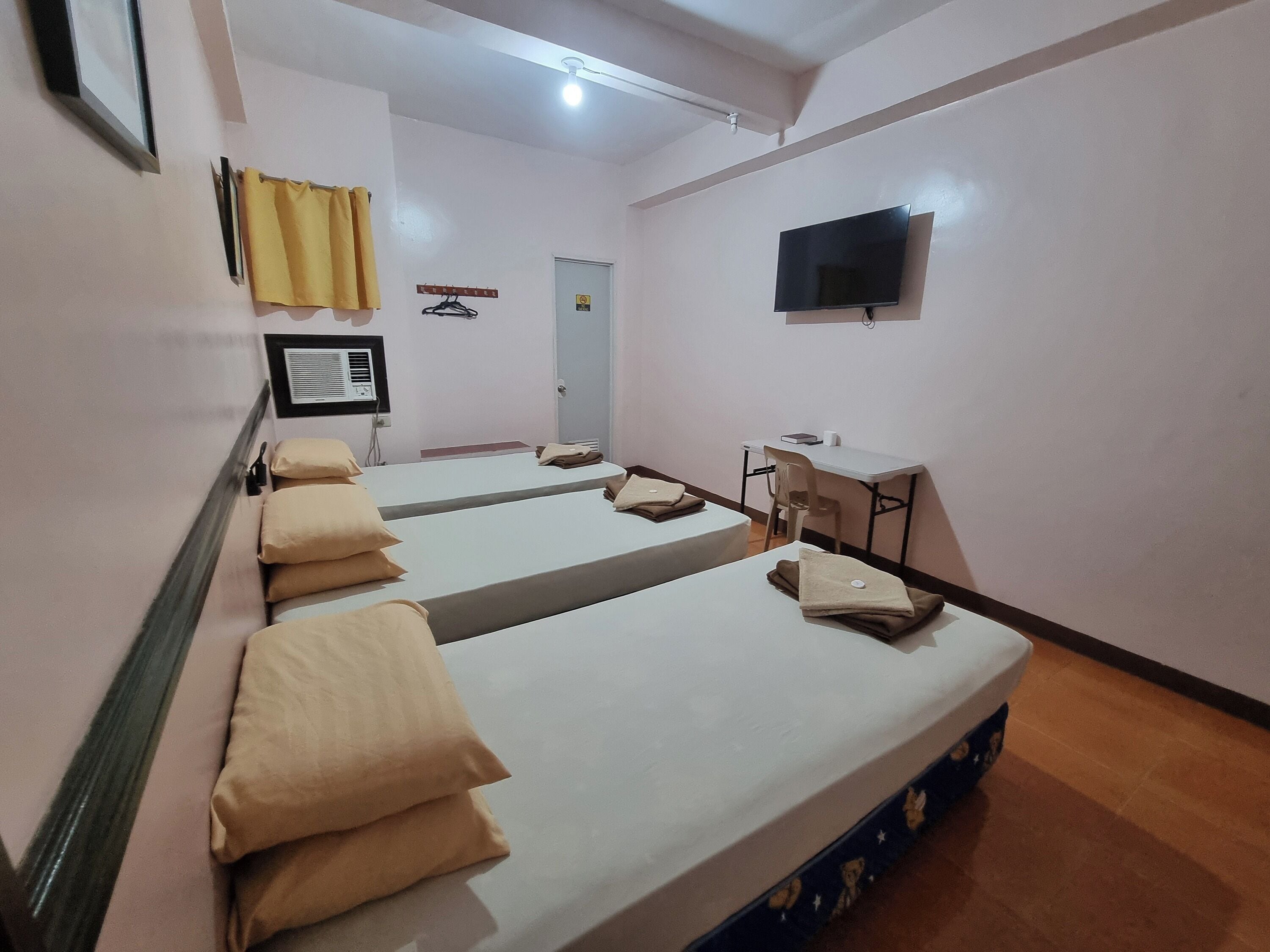 A hotel room with two beds, a desk, a chair, a television, and a window with curtains.