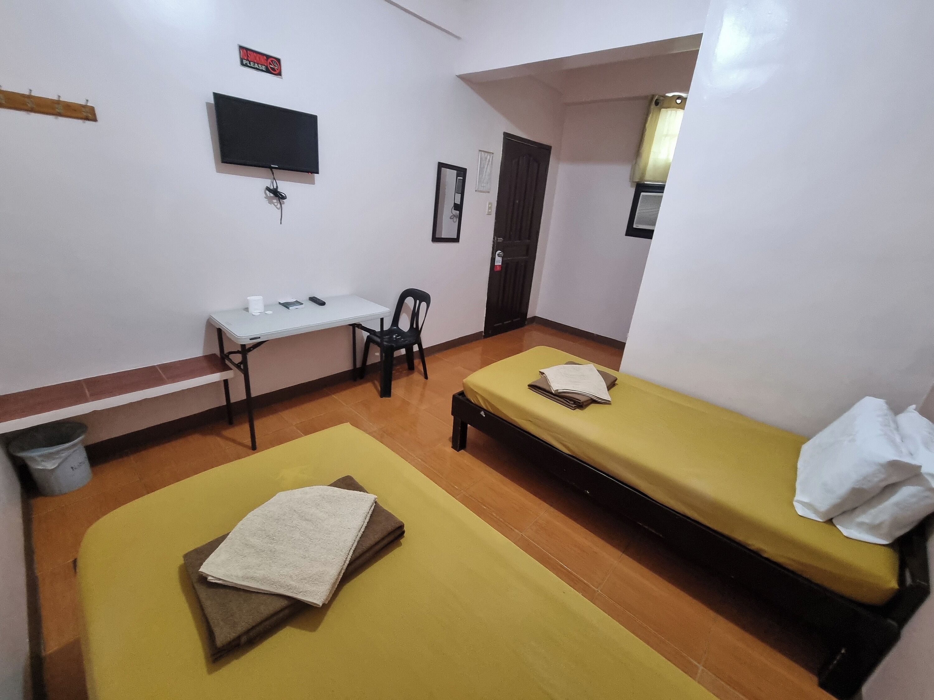 A room with a bed, a desk, a chair, a television, and a door.