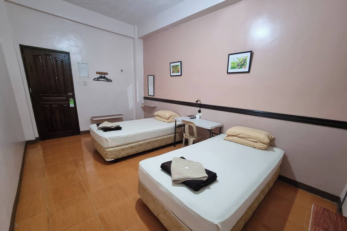 A hotel room with two beds, a desk, a chair, and a door.