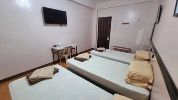 A hotel room with three single beds, a desk with a chair, a flat-screen TV, and a door.