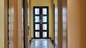 A hallway with a reflective tiled floor, a central door with glass panels, and wooden doors on either side. - Palm Woods Pensionne Home General Santos (General Santos)