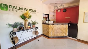 A reception area with a sign for Palm Woods Pension Home, a reception desk, a wall-mounted clock, and a bulletin board with notices. - Palm Woods Pensionne Home General Santos (General Santos)