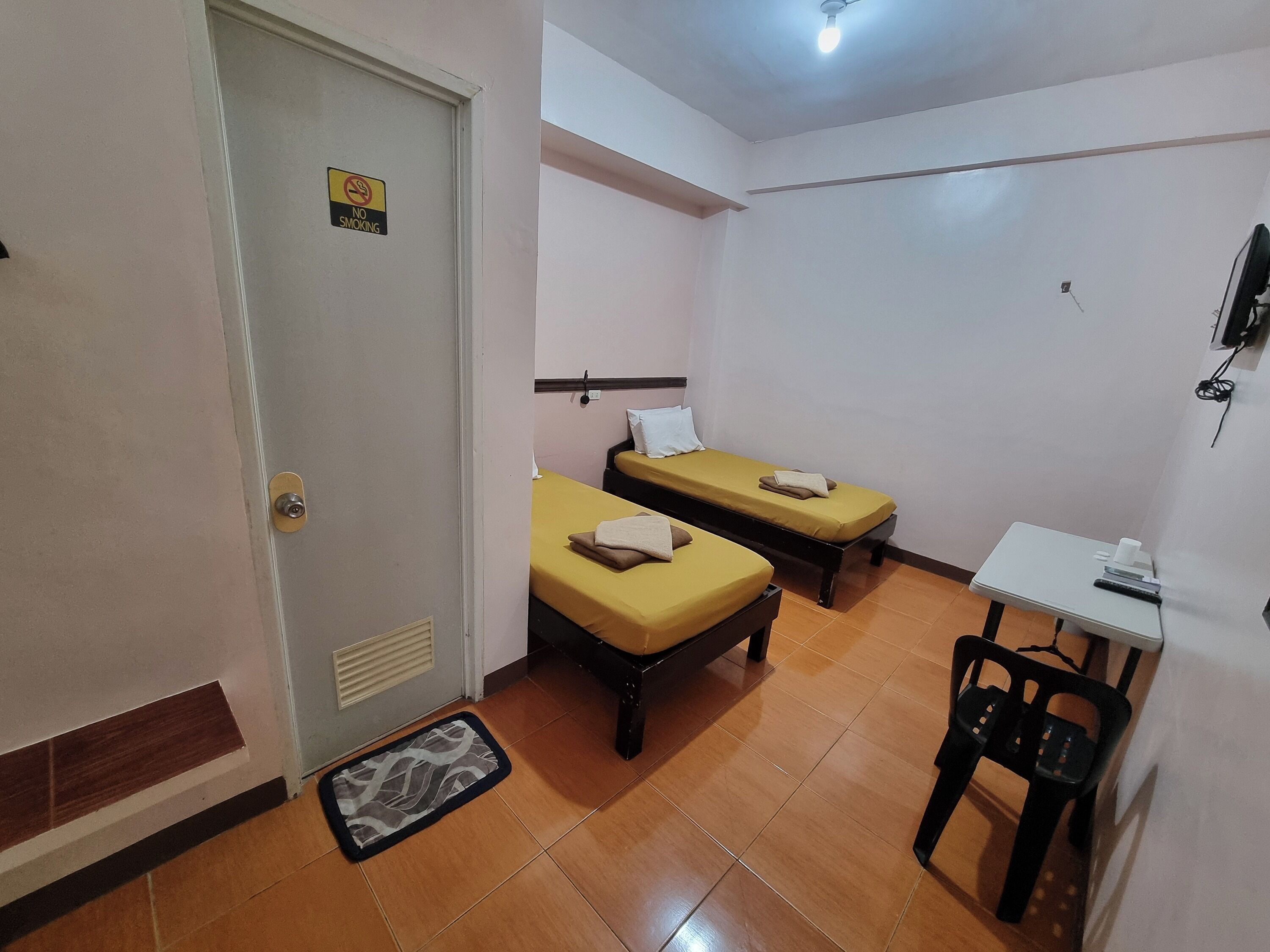 A small, clean room with two beds, a desk, and a chair.