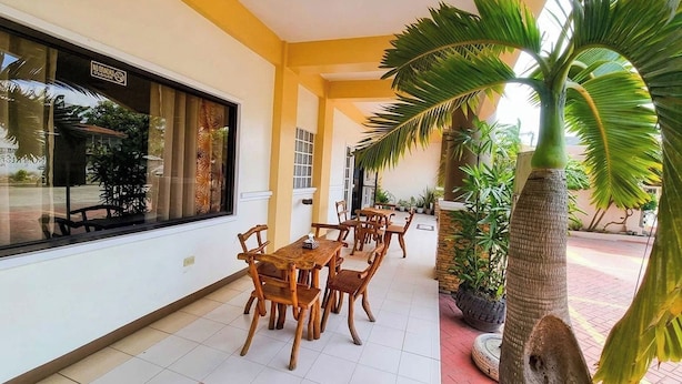 A covered outdoor dining area with wooden tables and chairs, potted plants, and a view through a window. - Palm Woods Pensionne Home General Santos (General Santos)