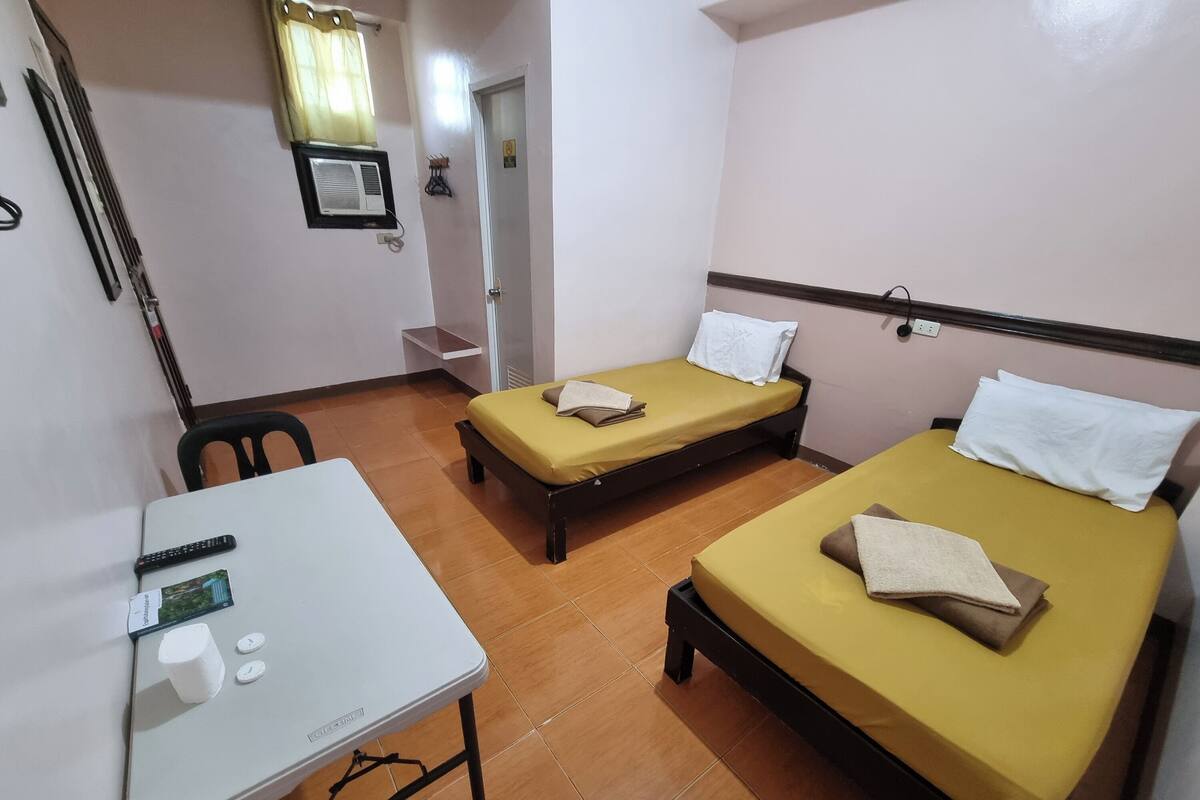 A room with two single beds, a small table with a remote control, and a chair.