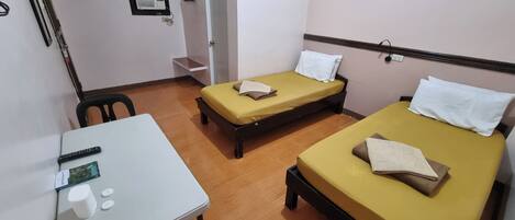 Una habitación con dos camas individuales, una mesita pequeña con un mando a distancia y una silla.