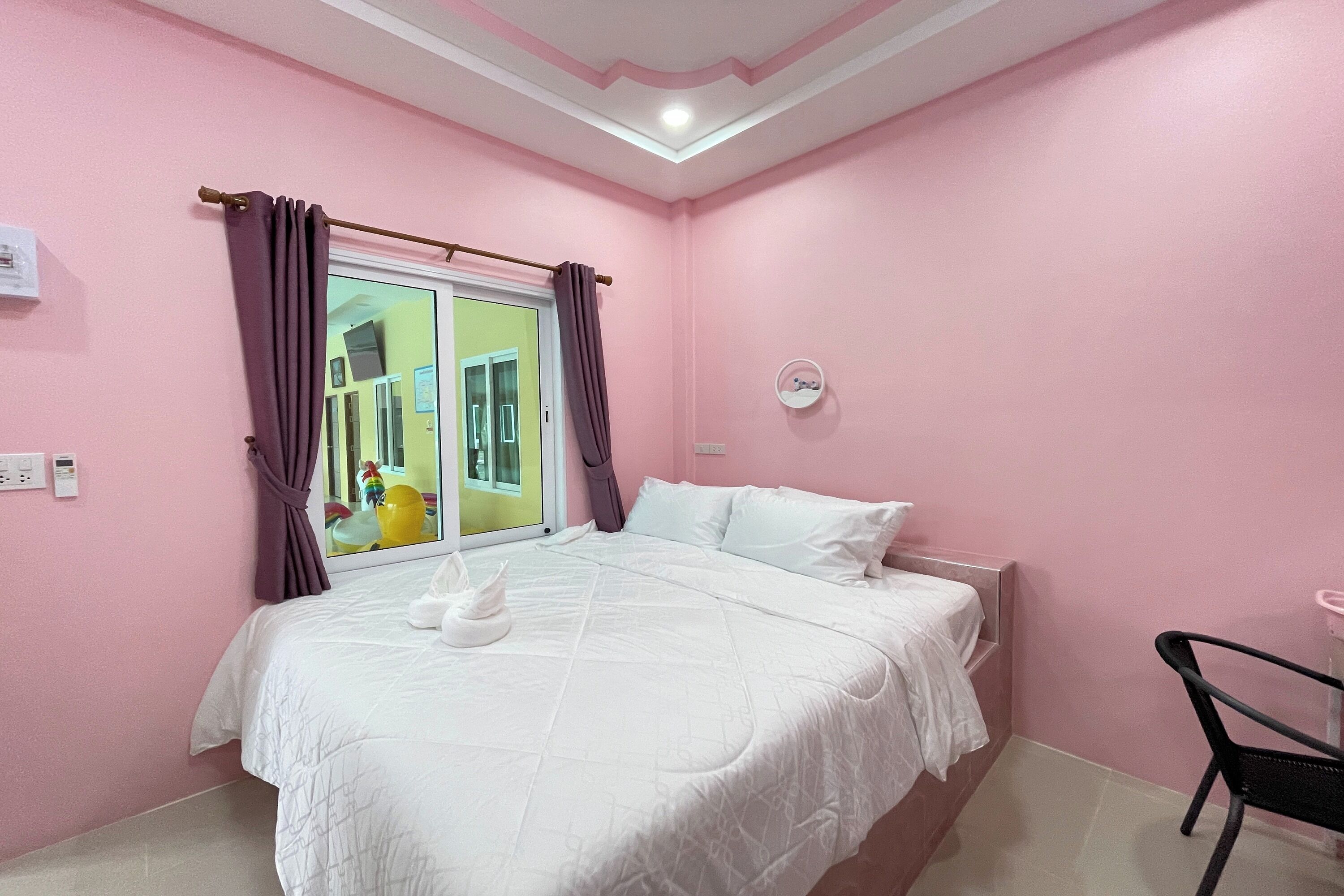 Ein Schlafzimmer mit rosa Wänden, einem Bett, einem Fenster mit violetten Vorhängen, einem kleinen runden Spiegel und einem Stuhl.