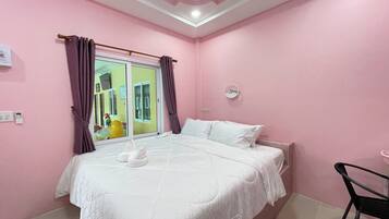 Ein Schlafzimmer mit rosa Wänden, einem Bett, einem Fenster mit violetten Vorhängen, einem kleinen runden Spiegel und einem Stuhl.