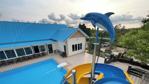 Une piscine avec un toboggan en forme de dauphin, un bâtiment avec un toit bleu et un sol à carreaux.