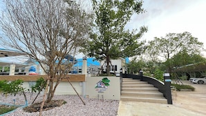 Une entrée d’immeuble avec un escalier, un arbre et un panneau portant le logo d’une maison et d’un arbre.