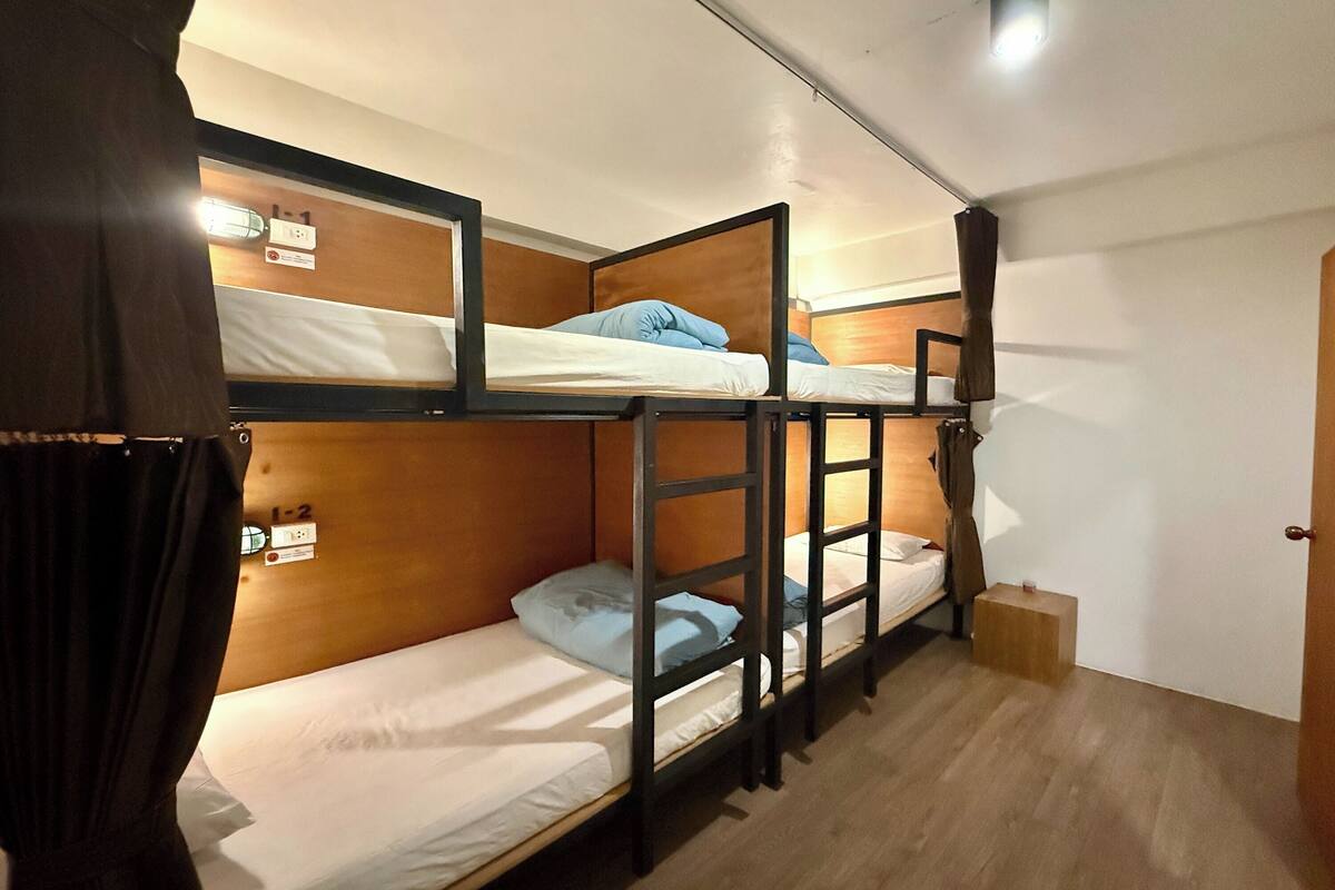 Quarto com beliches, paredes de madeira, porta e luminária no teto.