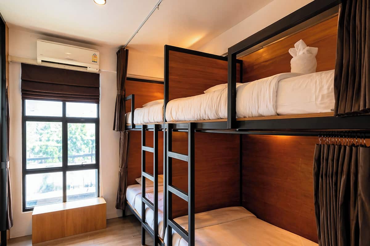 Quarto com beliche, janela, ar condicionado e um banco de madeira.